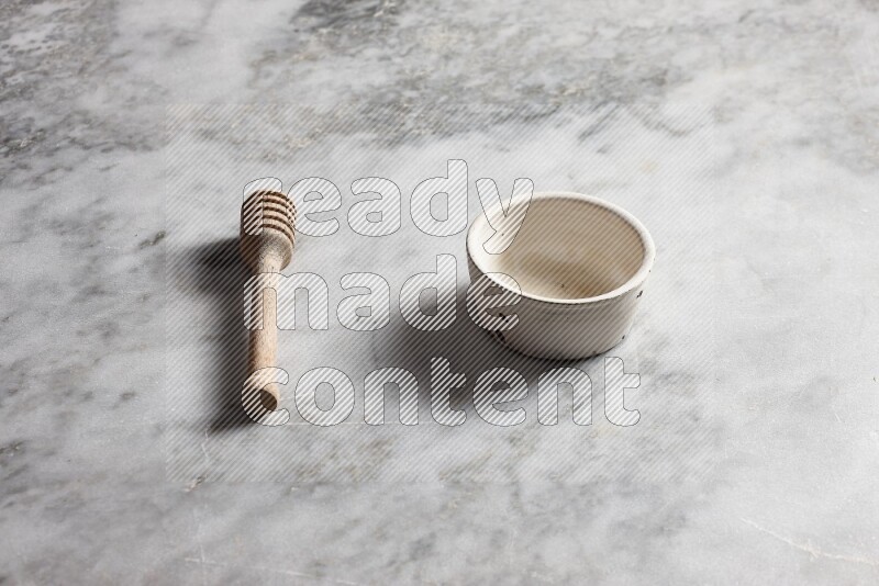 White pottery bowl with wooden honey dipper on the side on grey marble background
