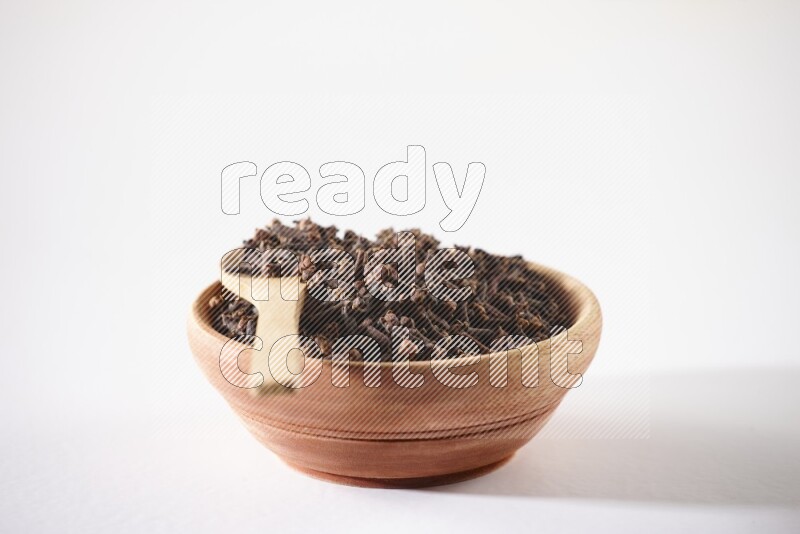 A wooden bowl and a wooden spoon full of cloves on a white flooring