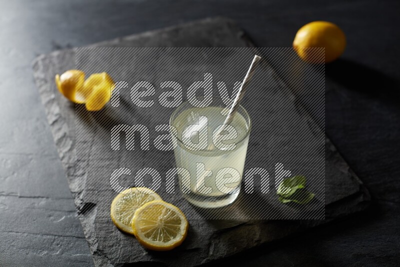 A glass of lemon juice with a straw on black background