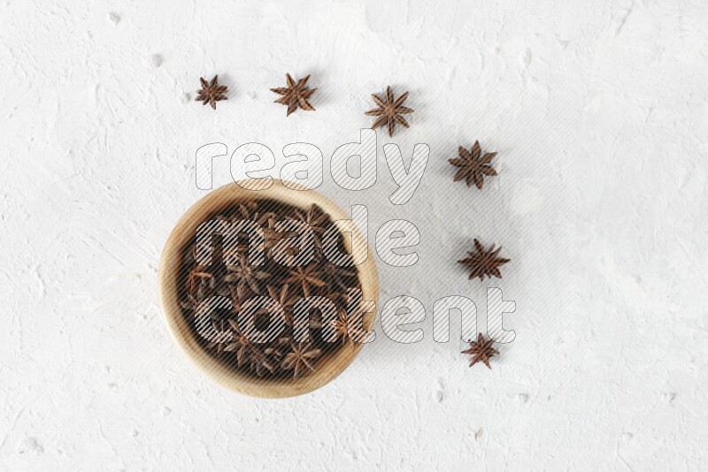 Star anise in a wooden bowl with more anise on the floor on white background
