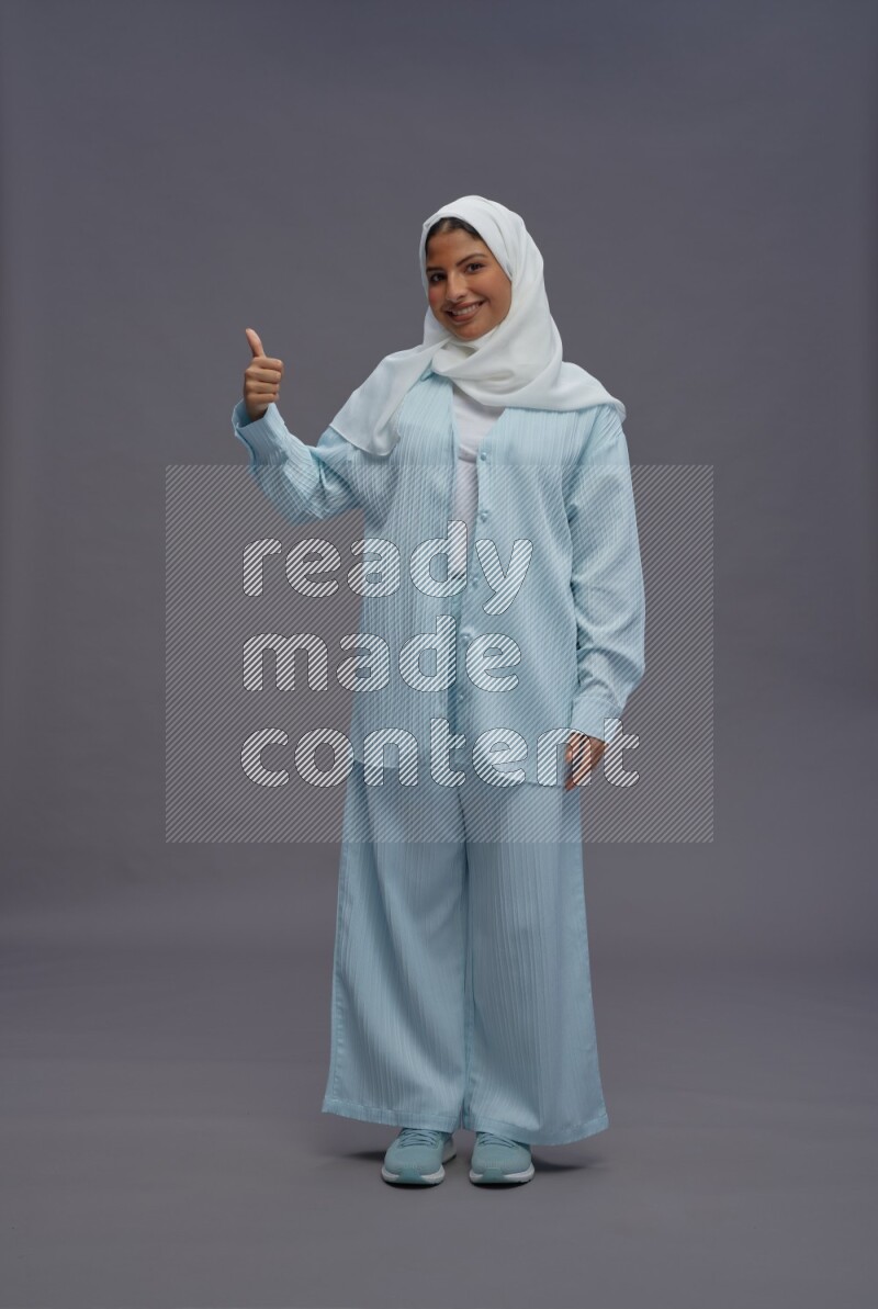 Saudi woman wearing hijab clothes standing interacting with the camera on gray background