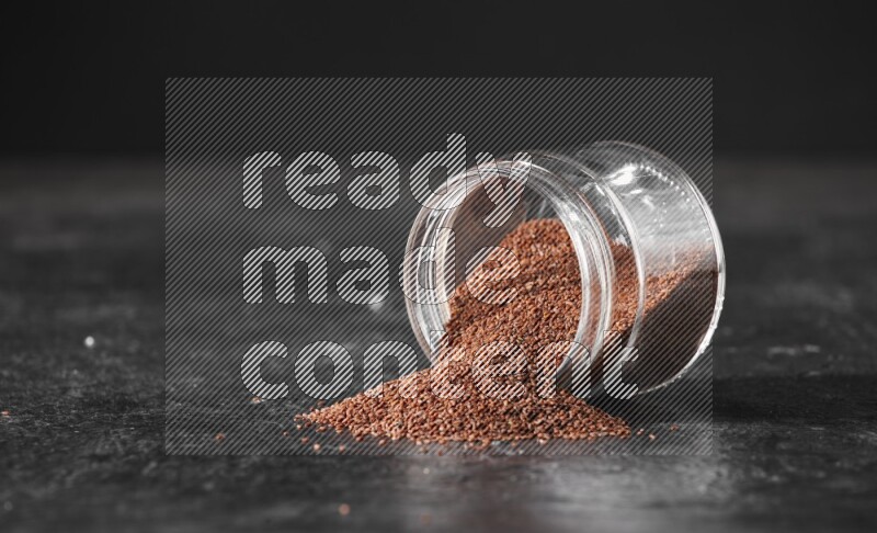 A glass jar full of garden cress seeds flipped and seeds spread out on a textured black flooring