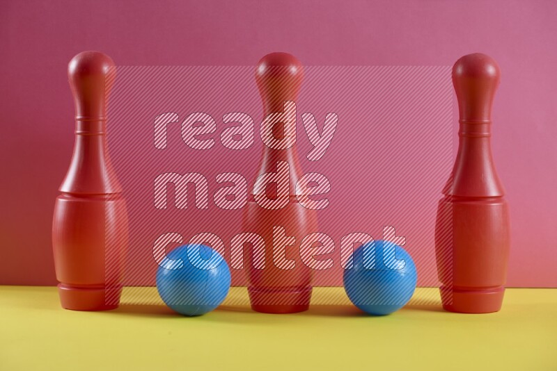 Plastic bowling pins with balls on pink and yellow background (kids toys)