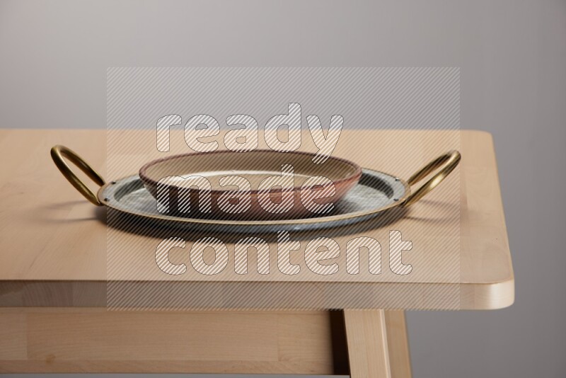 multicolored plate placed on a rounded stainless steel tray with golden handels on the edge of wooden table