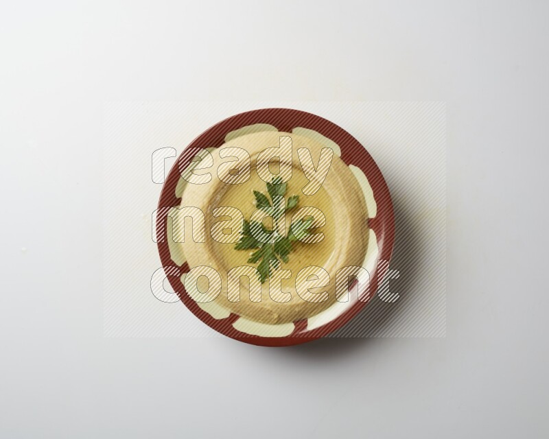 Hummus in a traditional plate garnished with parsley on a white background