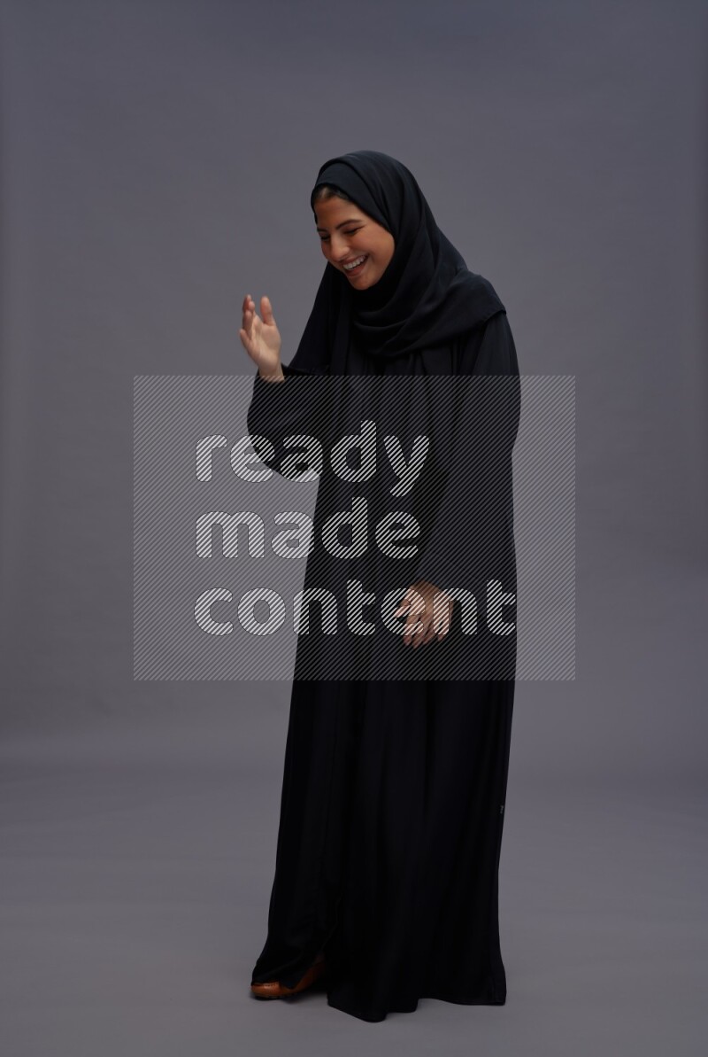 Saudi woman wearing Abaya standing interacting with the camera on gray background