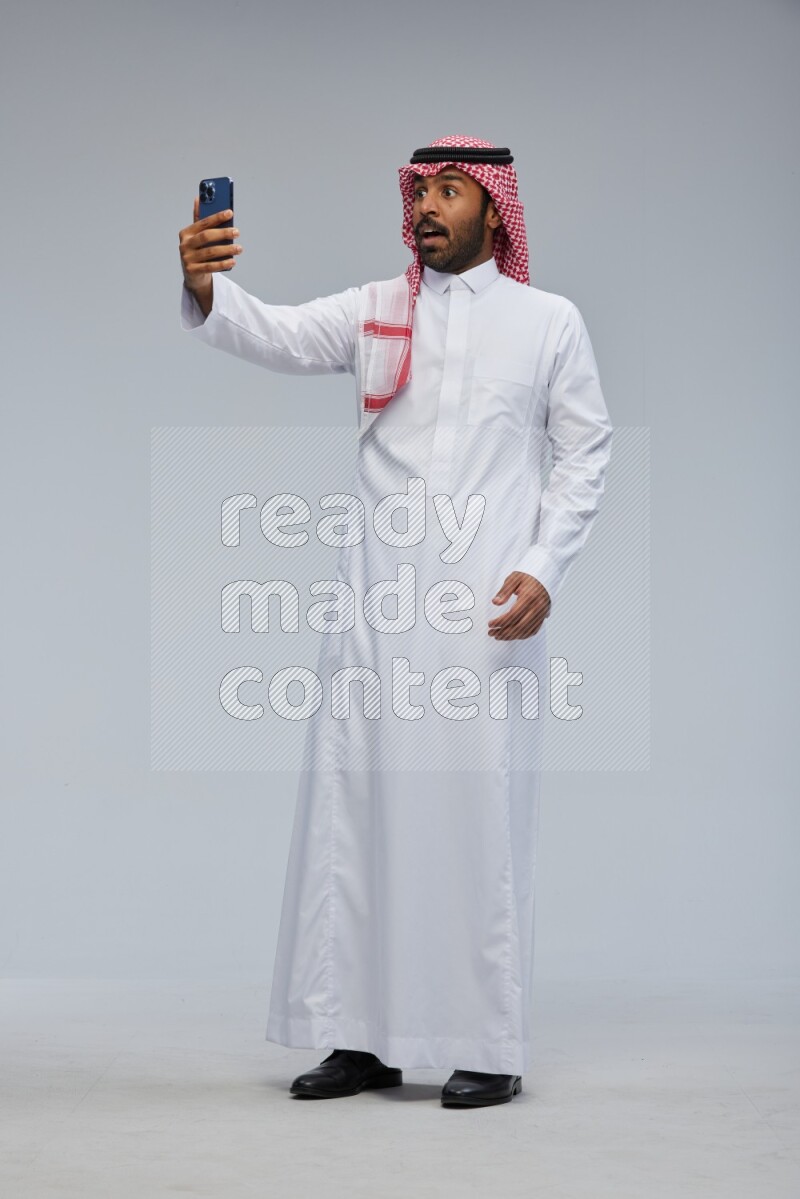 Saudi man Wearing Thob and shomag standing taking selfie on Gray background