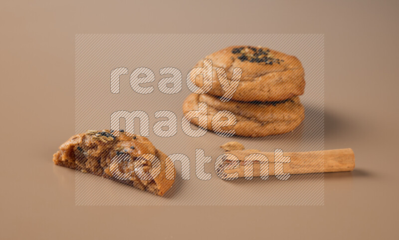 Three chocolate chip cookies beside cinimon sticks on a brown background
