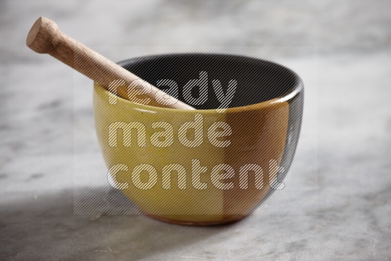 Multicolored pottery bowl with wooden honey dipper in it on grey marble background