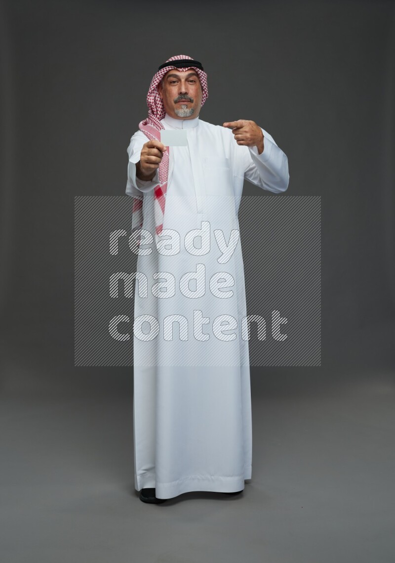 Saudi man with shomag Standing holding ATM card on gray background
