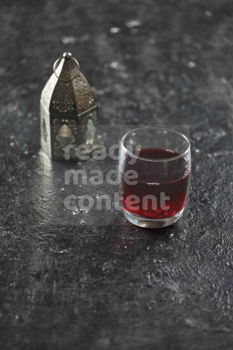 A silver lantern with different drinks, dates, nuts, prayer beads and quran on textured black background