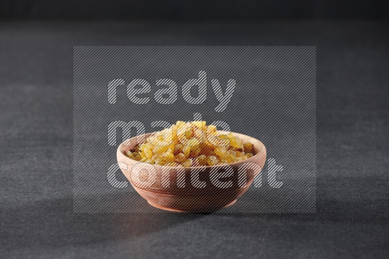 A wooden bowl full of raisins on a black background in different angles