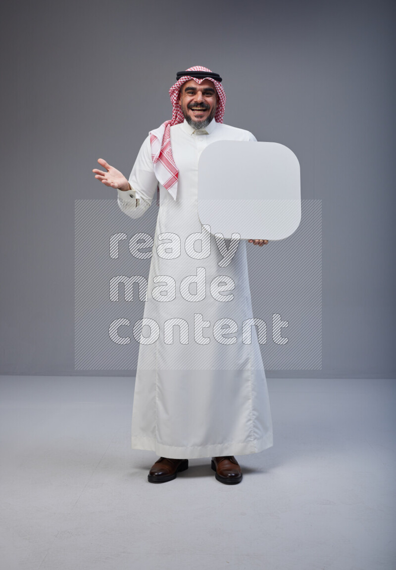 Saudi man Wearing Thob and red Shomag standing holding social media sign on Gray background
