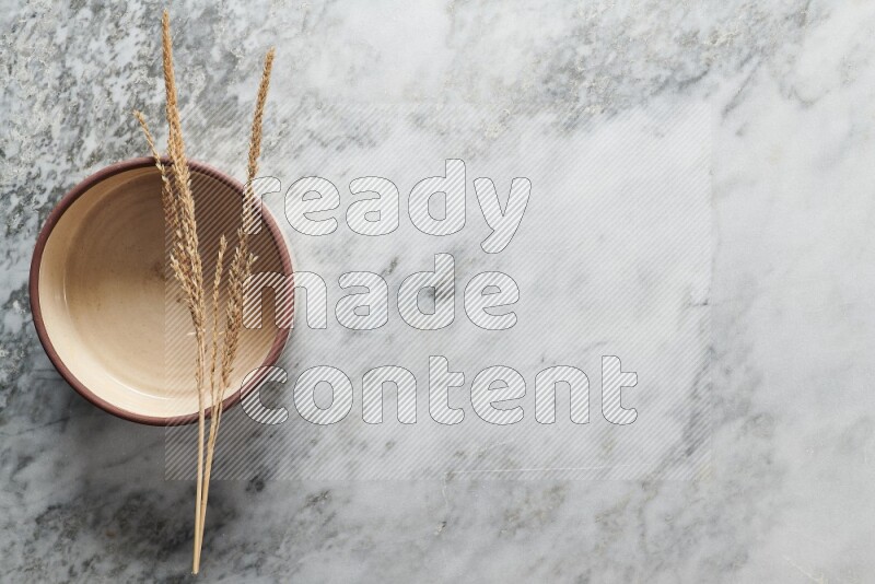 Wheat stalks on beige pottery oven bowl on grey marble background