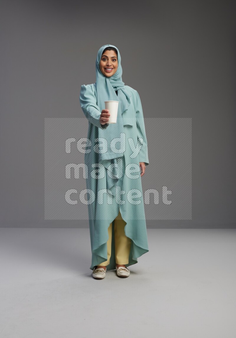 Saudi Woman wearing Abaya standing  holding paper cup on Gray background