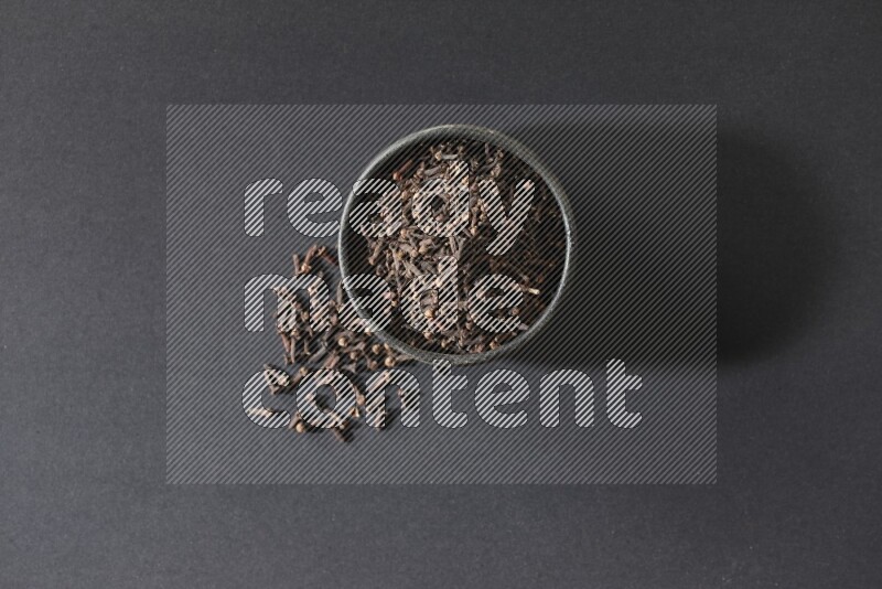A black pottery bowl full of cloves on a black flooring