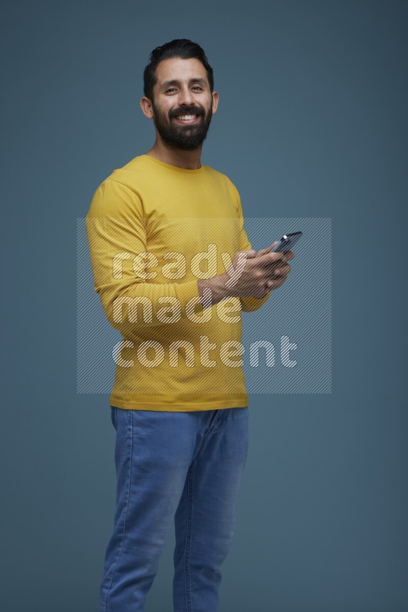 Man posing with a phone in a blue background wearing a yellow shirt