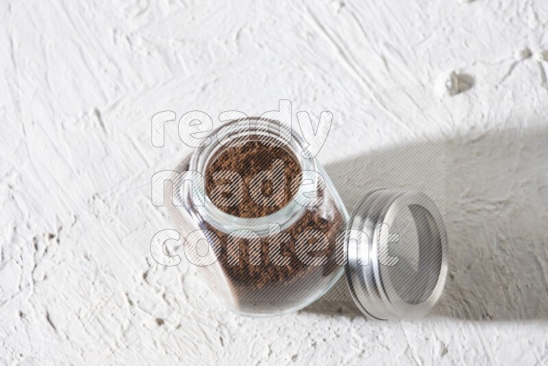 A glass spice jar full of cloves powder on textured white flooring