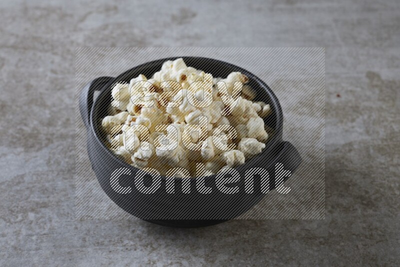 popcorn in a black handheld ceramic bowl on a grey textured countertop