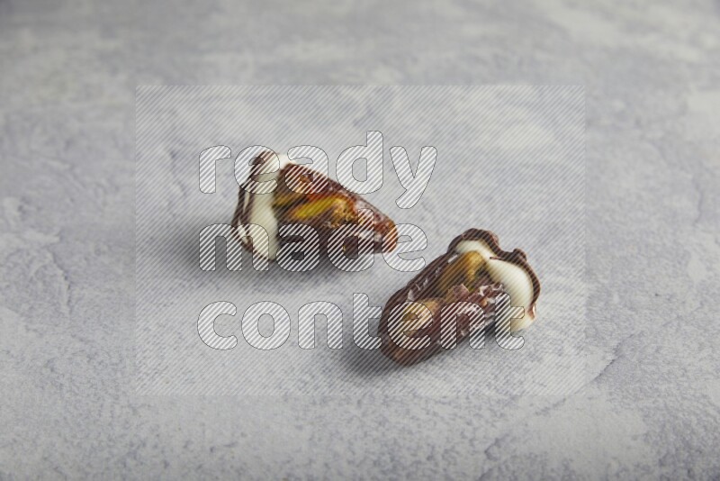 two pistachio stuffed dates covered with white chocolate with dark chocolate drizzle on a light grey background