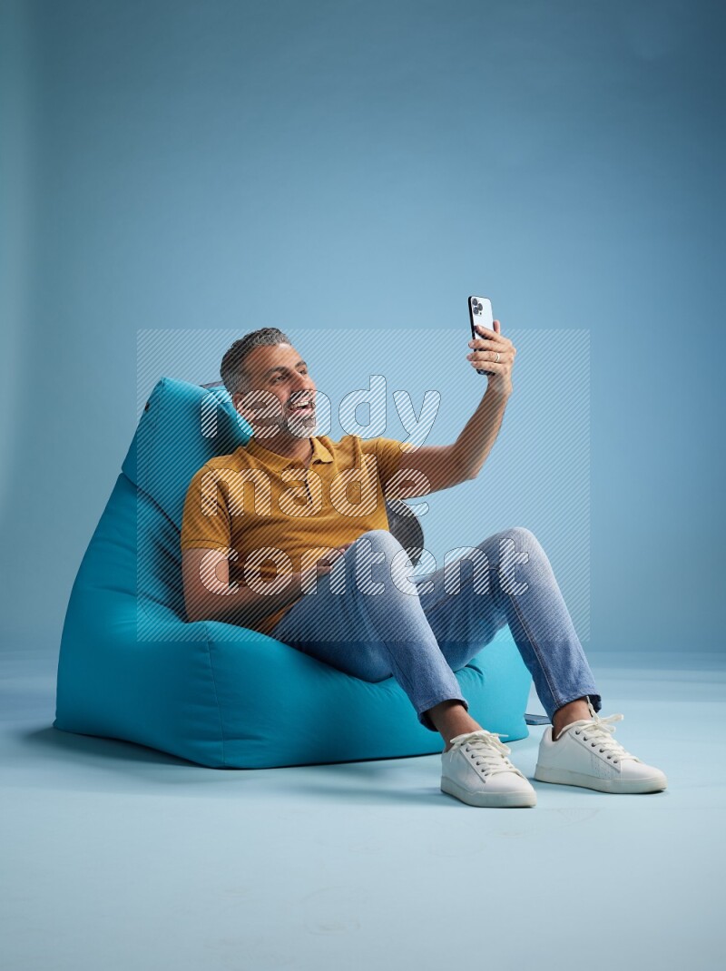 A man sitting on a blue beanbag and taking selfie
