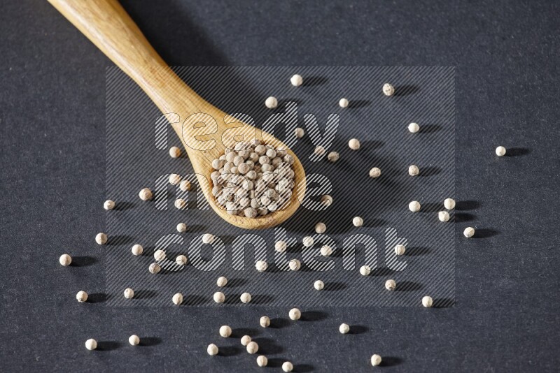 A wooden spoon full of white pepper beads on black flooring