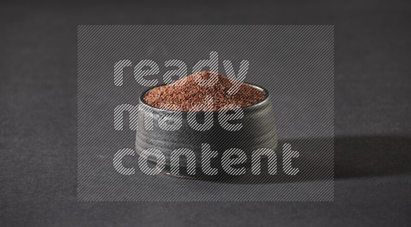 A black pottery bowl full of garden cress seeds on a black flooring