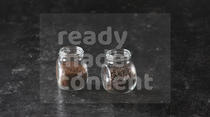 Glass spice jars full of cloves and cloves powder on textured black flooring