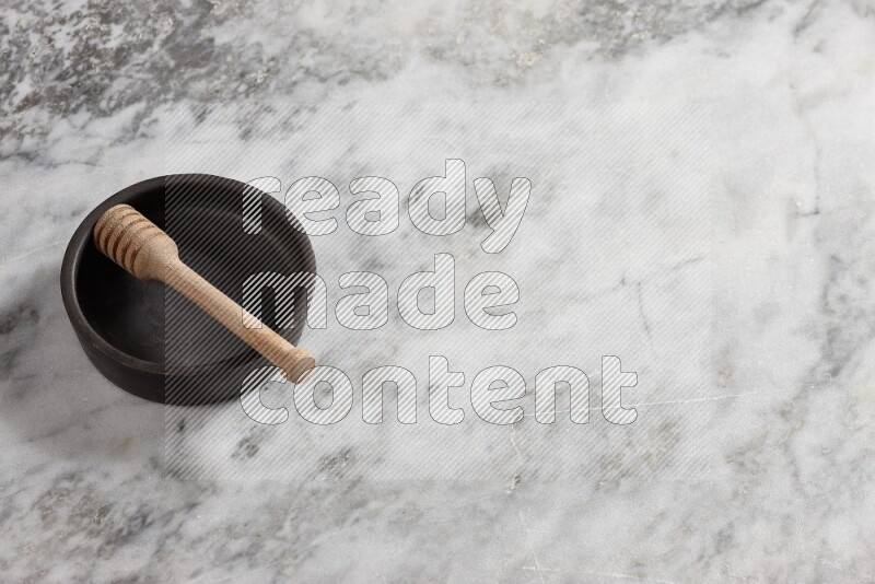 Black pottery bowl with wooden honey dipper in it on grey marble background