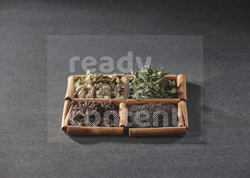 4 مربعات من عيدان القرفة ممتلئة بالشاي الأسود والقرنفل والنعناع المجفف وحبوب الهيل على أرضية سوداء