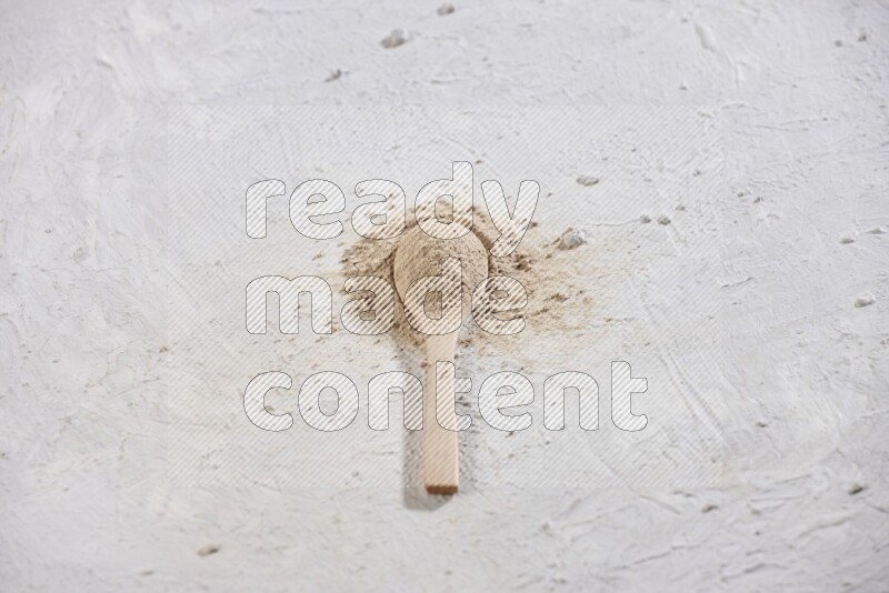 A wooden spoon full of garlic powder with scattered powder around it on a textured white flooring
