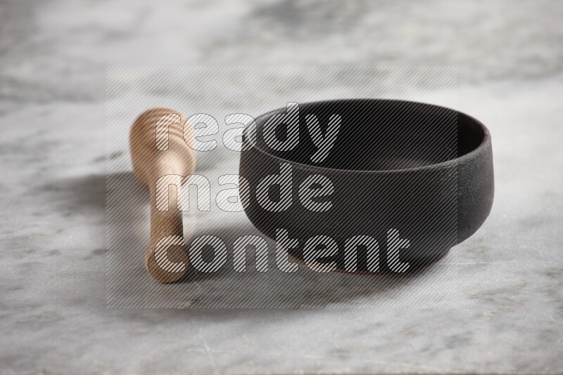 Black pottery bowl with wooden honey dipper on the side on grey marble background