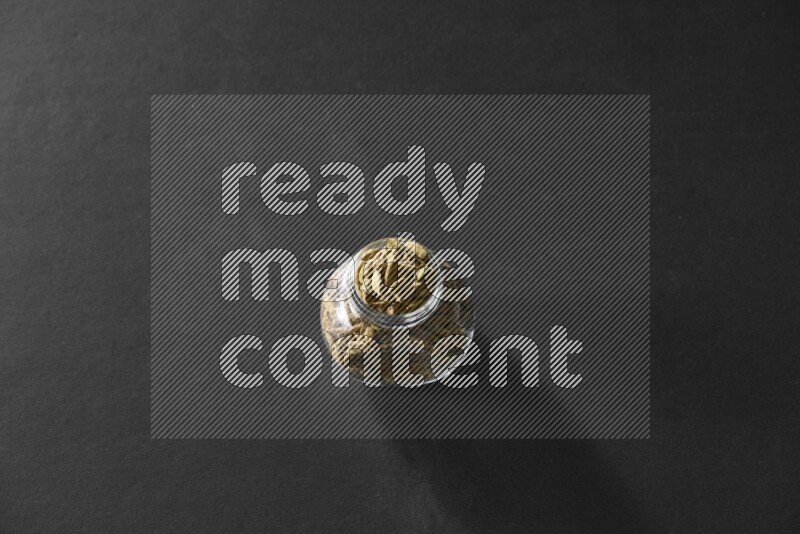 A glass spice jar full of cardamom on black flooring