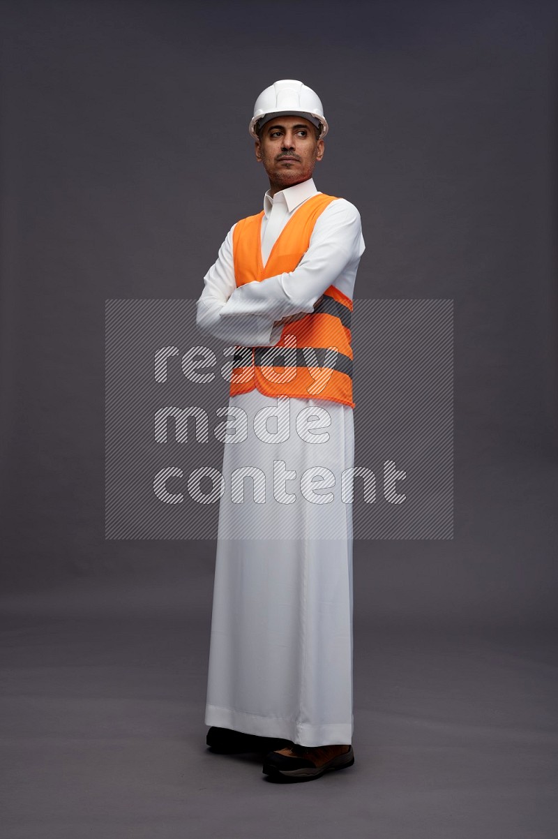 Saudi man wearing thob with engineer vest standing with crossed arms on gray background