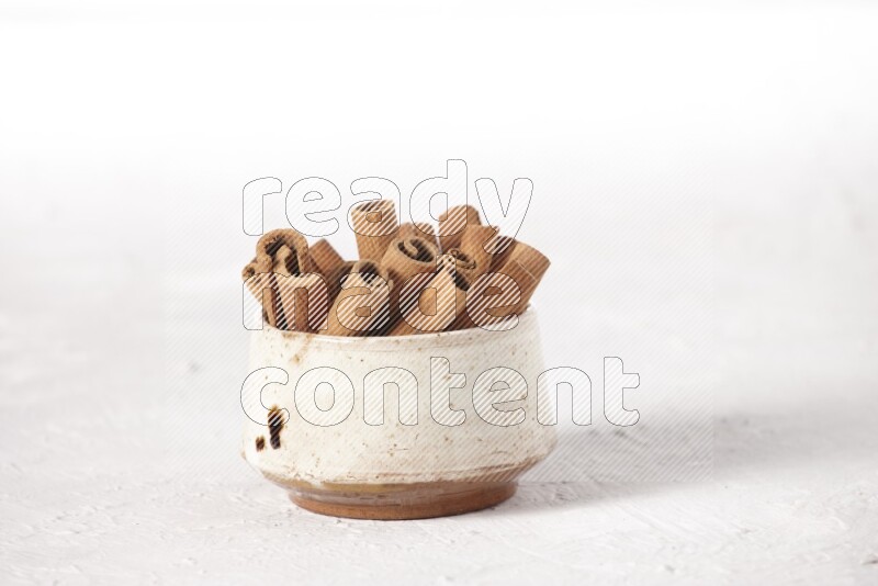 Cinnamon sticks in a beige bowl on a white background