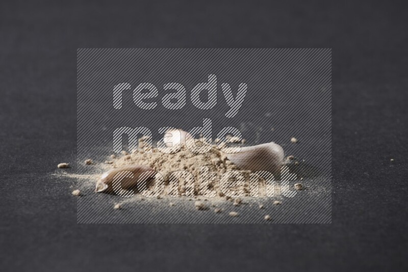 A small pile of garlic powder with some of cloves and a whole garlic bulb on a black flooring