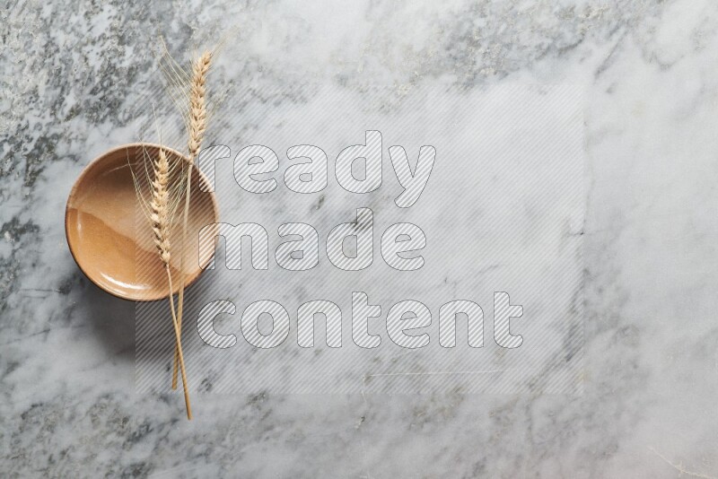 Wheat stalks on multicolored pottery plate on grey marble background