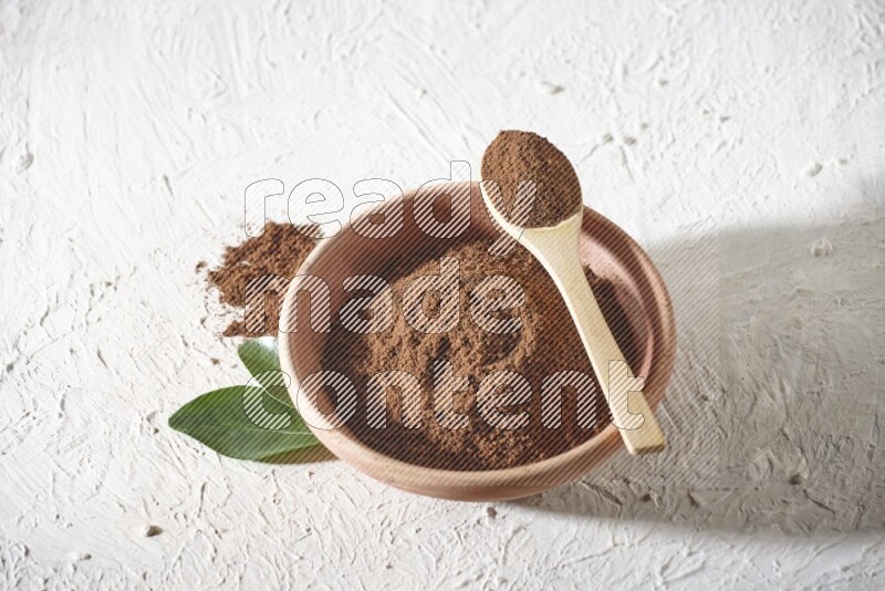 A wooden bowl and a wooden spoon full of cloves powder on a textured white flooring