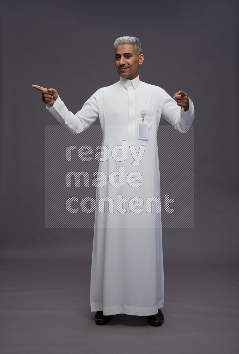 Saudi man wearing thob with pocket employee badge standing interacting with the camera on gray background