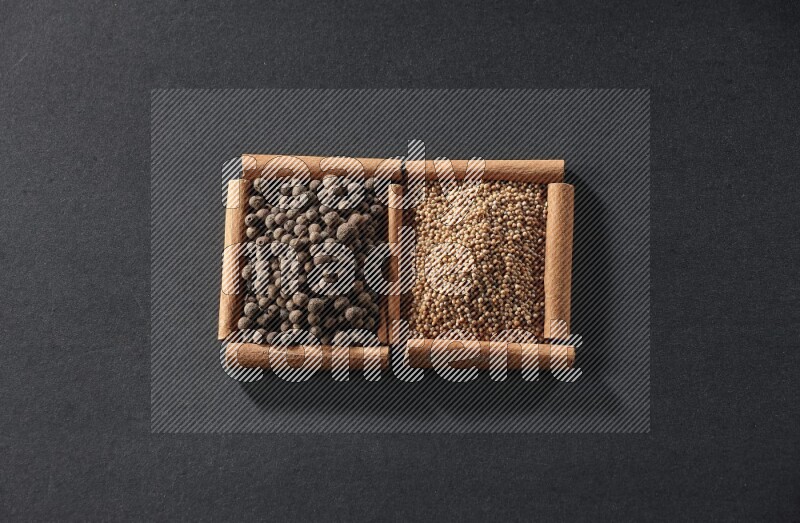 مربعان من أعواد القرفة ممتلئان بحبوب الخردل وحبوب بهار الفلفل الحلو علي خلفية سوداء