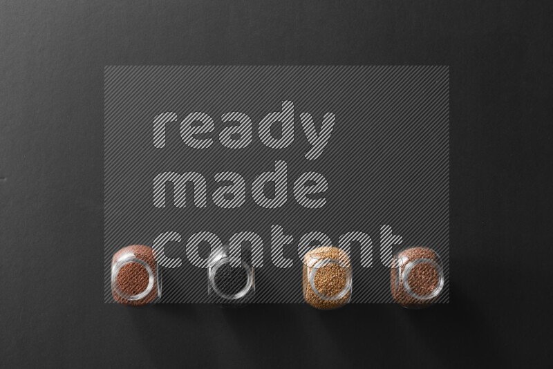 4 glass spice jars full of black seeds, mustard seeds, flax and garden cress on black flooring