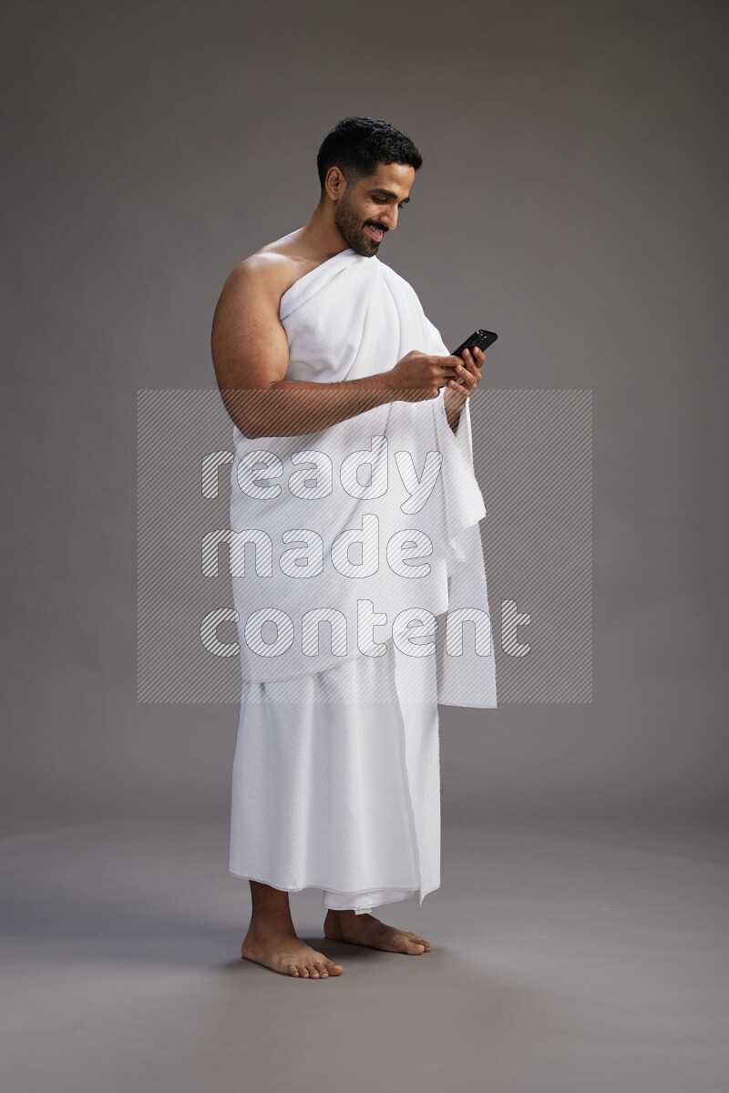 A man wearing Ehram Standing texting on phone on gray background
