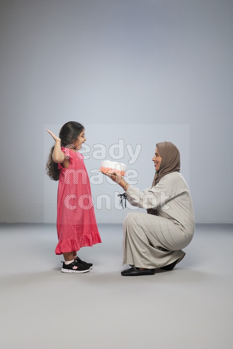 A mother giving a cake to her daughter on gray background