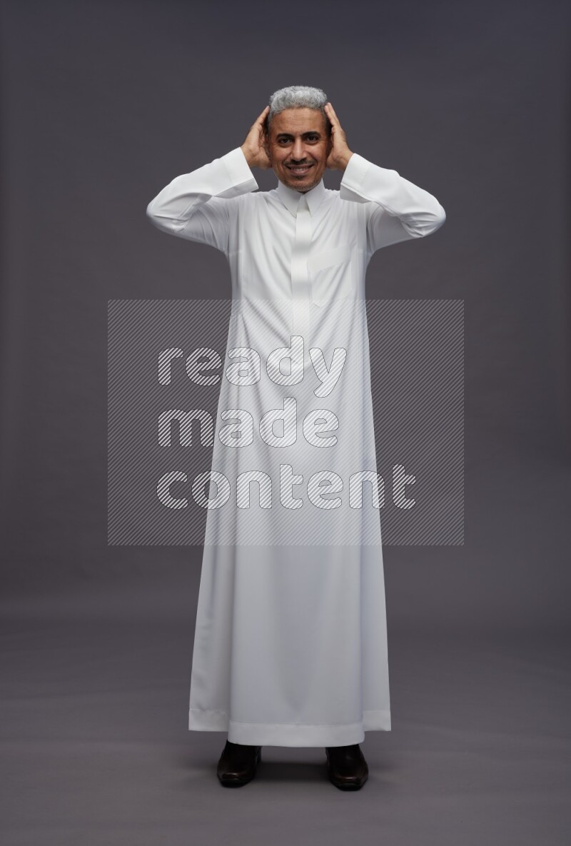 Saudi man wearing thob standing hands behind head on gray background