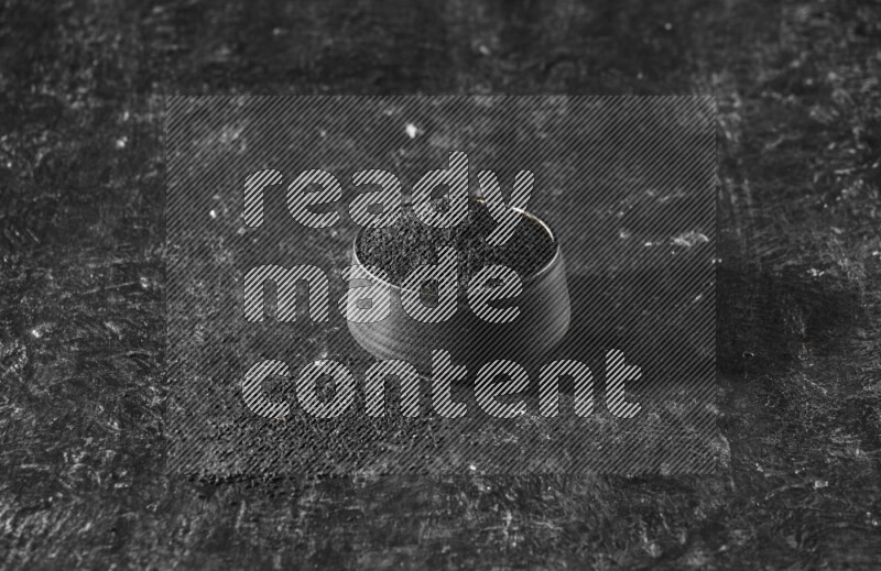 A black pottery bowl full of black seeds on a textured black flooring