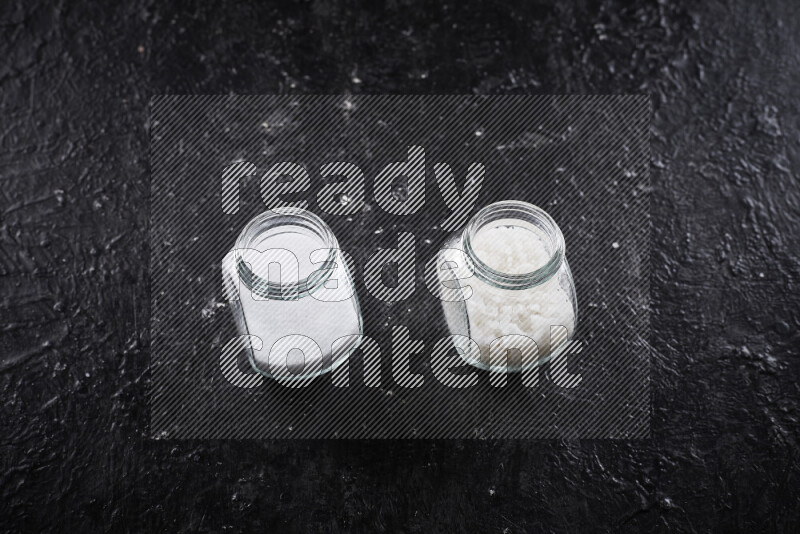 2 وعاء زجاجي احدهمها ممتلئ بملح الطعام الأبيض والأخر بملح البحر الخشن على خلفية سوداء