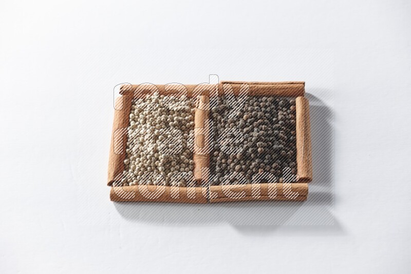 2 squares of cinnamon sticks full of black pepper and white pepper on white flooring