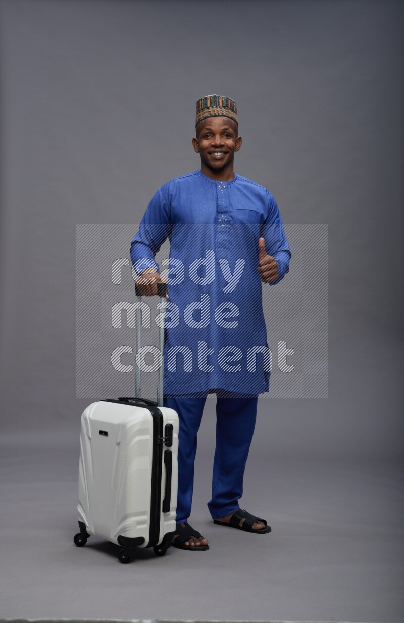 Man wearing Nigerian outfit standing holding bag on gray background