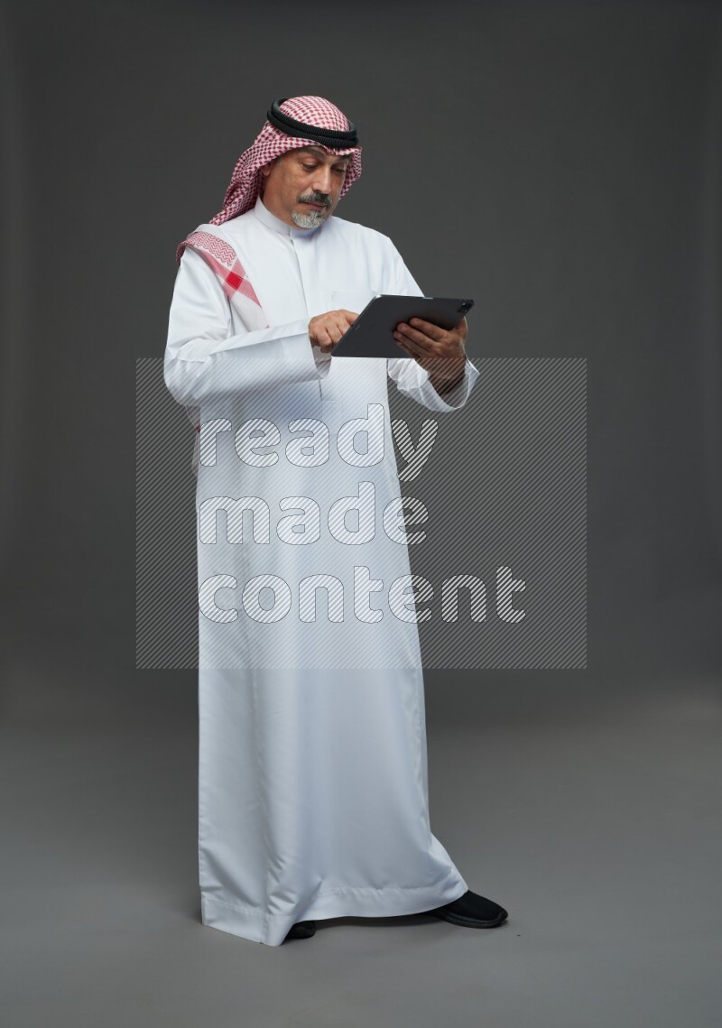 Saudi man with shomag Standing working on tablet on gray background