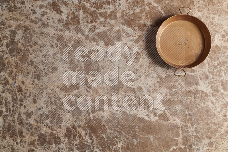 A small copper pan on beige marble background